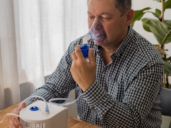 Elderly,Man,Sitting,On,A,Table,And,Using,A,Nebulizer
